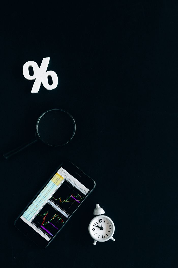 Bookkeeping Services Smartphone displaying stock market charts with a magnifying glass and clock on a black background.